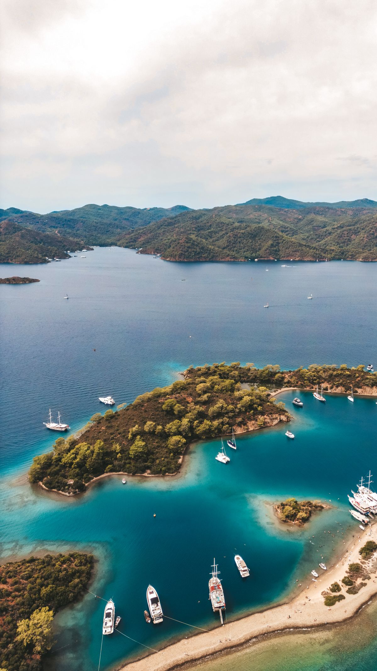 A wooden day boat anchored in clear turquoise water beside small pine-covered islands in the Gulf of Fethiye with swimmers in the sea